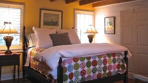 A bedroom with a bed, two bedside lamps, a window with blinds, and a door. - Historic Cottage on Ware River Estate (Gloucester)