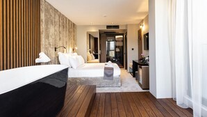 Een moderne hotelkamer met een houten vloer, een groot bed met witte lakens, een nachtkastje, een bureau met stoel, en een grote spiegel.