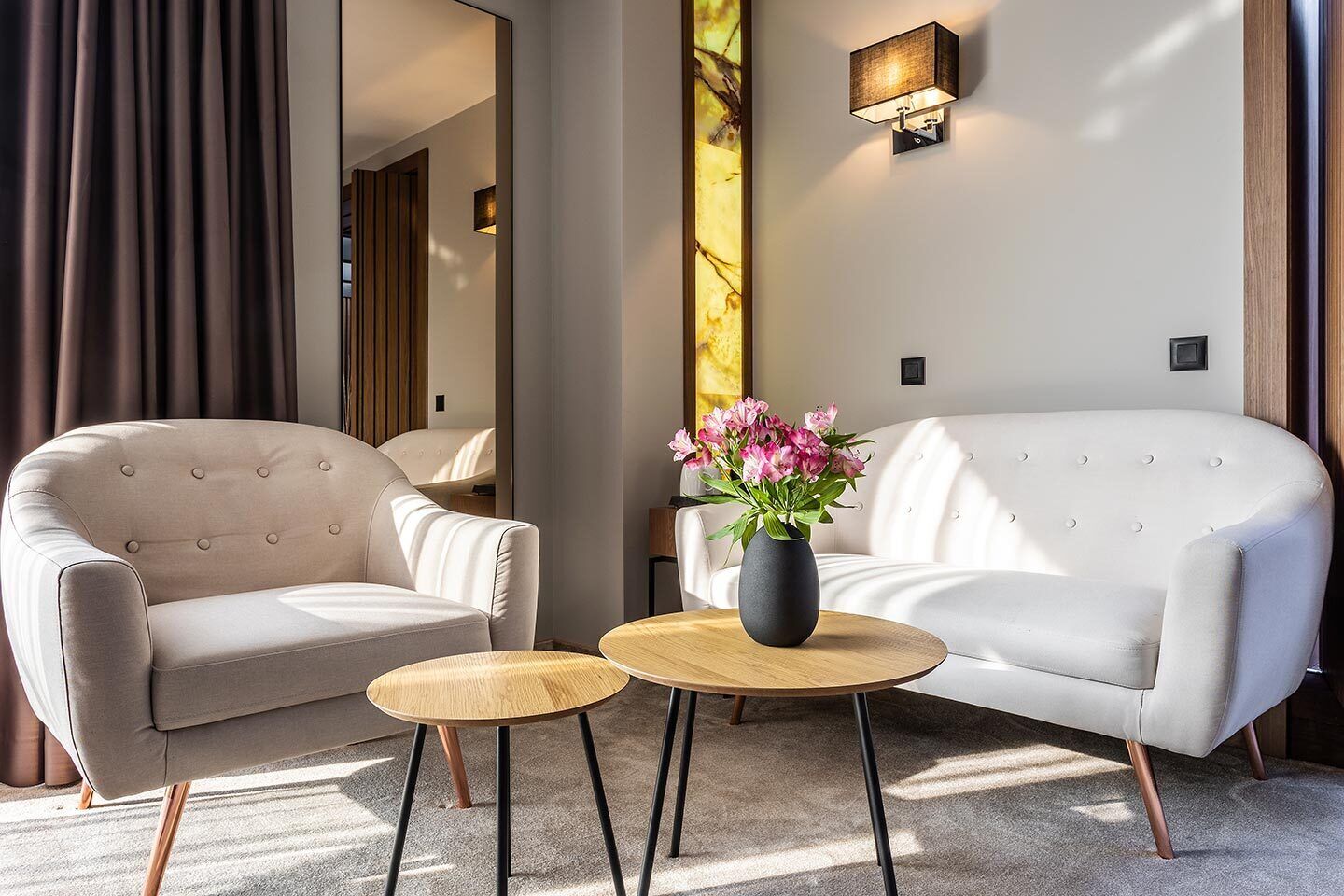 A modern living room with a beige sofa, a matching armchair, and a small wooden coffee table with a vase of flowers.