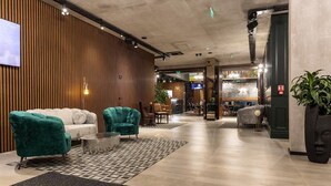 Een moderne lobby met een houten accentmuur, een zithoek met smaragdgroene en witte banken, en een receptiebalie.