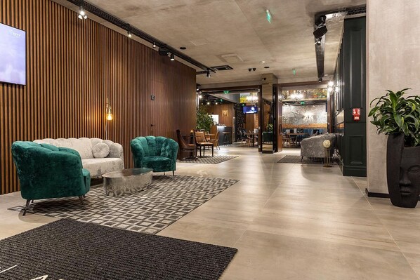 Een moderne lobby met een houten accentmuur, een zithoek met smaragdgroene en witte banken, en een receptiebalie.