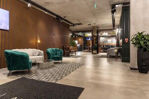 A modern lobby with a wooden accent wall, a seating area with teal and white sofas, and a reception desk.