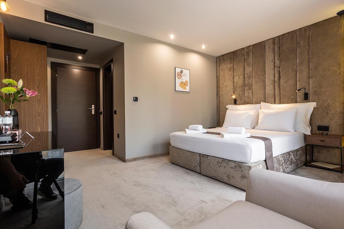 A modern hotel room with a bed, bedside table, and a desk with a chair.