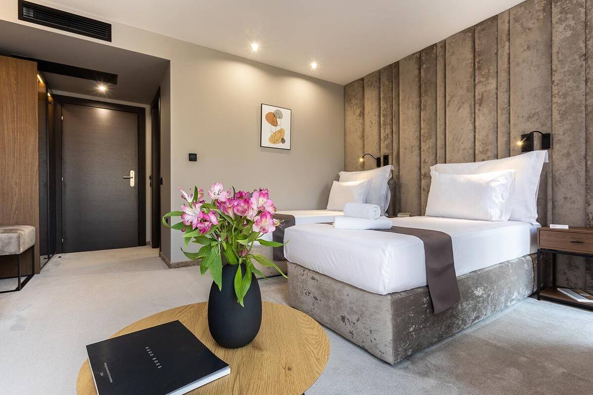 A modern hotel room with a large bed, a bedside table, a small desk, and a vase of flowers.