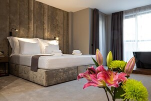 Una habitación de hotel moderna con una cama grande, un revestimiento de pared de madera, un escritorio con lámpara y vistas a la ciudad a través de amplias ventanas.