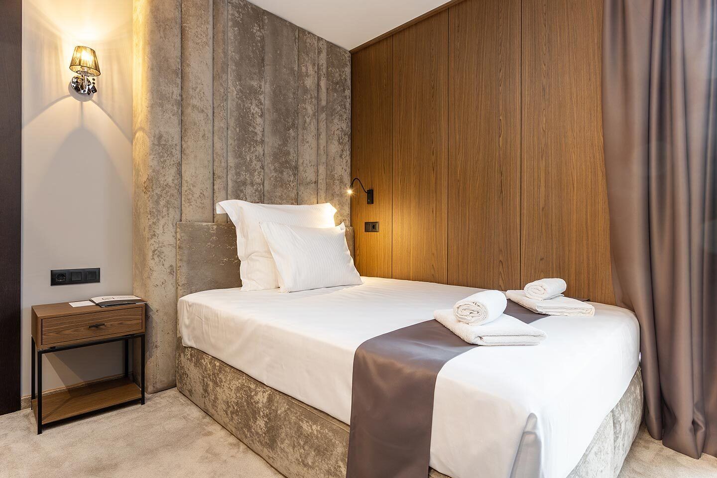 Une chambre d’hôtel moderne avec un grand lit, une table de chevet, une lampe fixée au mur et un mur décoratif en bois.