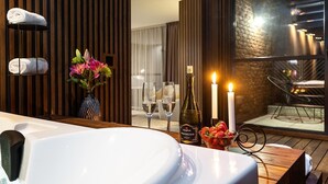 Een moderne badkamer met een groot bad, handdoeken, een vaas met bloemen, twee wijnglazen, een flesje Prosecco en twee brandende kaarsen.