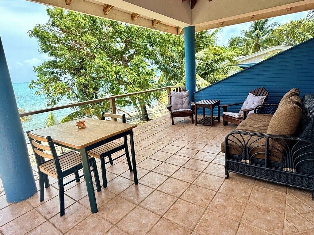 Ein überdachter Außenbereich zum Sitzen mit Tisch, Stühlen und einer Couch, mit Blick auf das Meer.