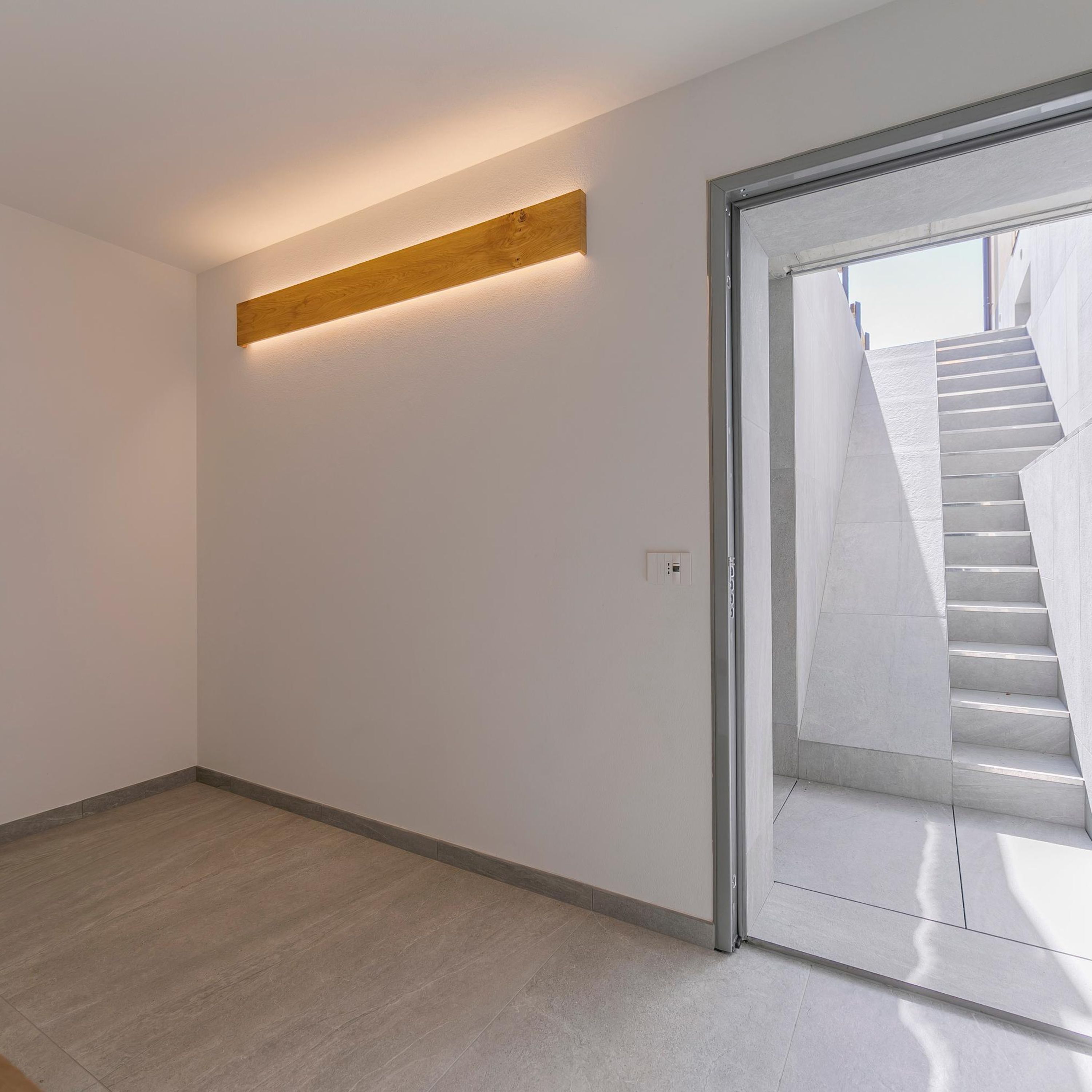 Un intérieur moderne avec un mur d’accent en bois, un escalier menant à un niveau supérieur et un interrupteur sur le mur.