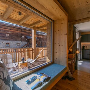 Ein Interieur einer Holzhütte mit einem großen Fenster, einer Leseecke mit einer Zeitschrift und einer Holztreppe, die nach draußen führt.