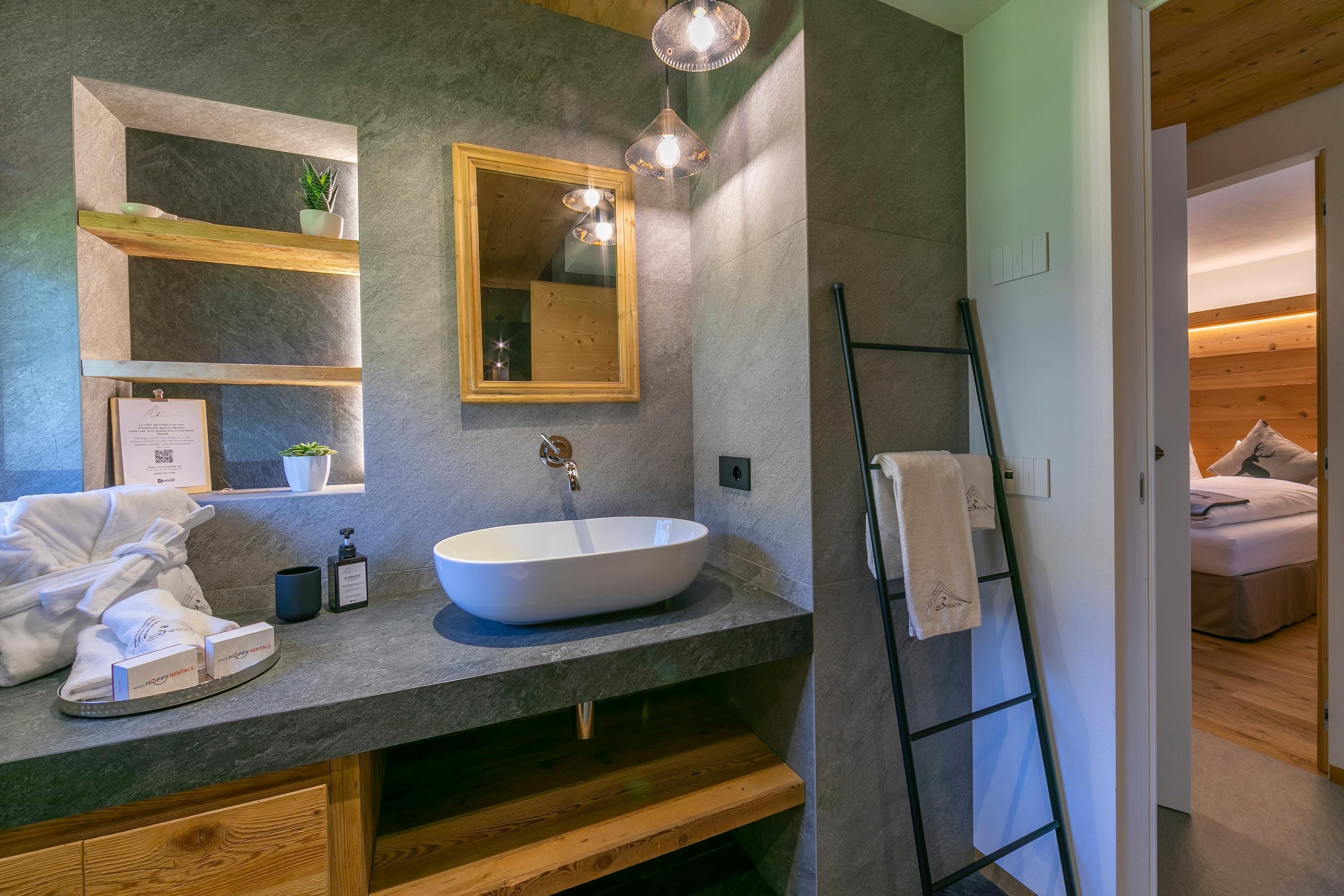 Ein modernes Badezimmer mit großem Spiegel, einem runden Waschbecken und einem Holzregal mit Toilettenartikeln.
