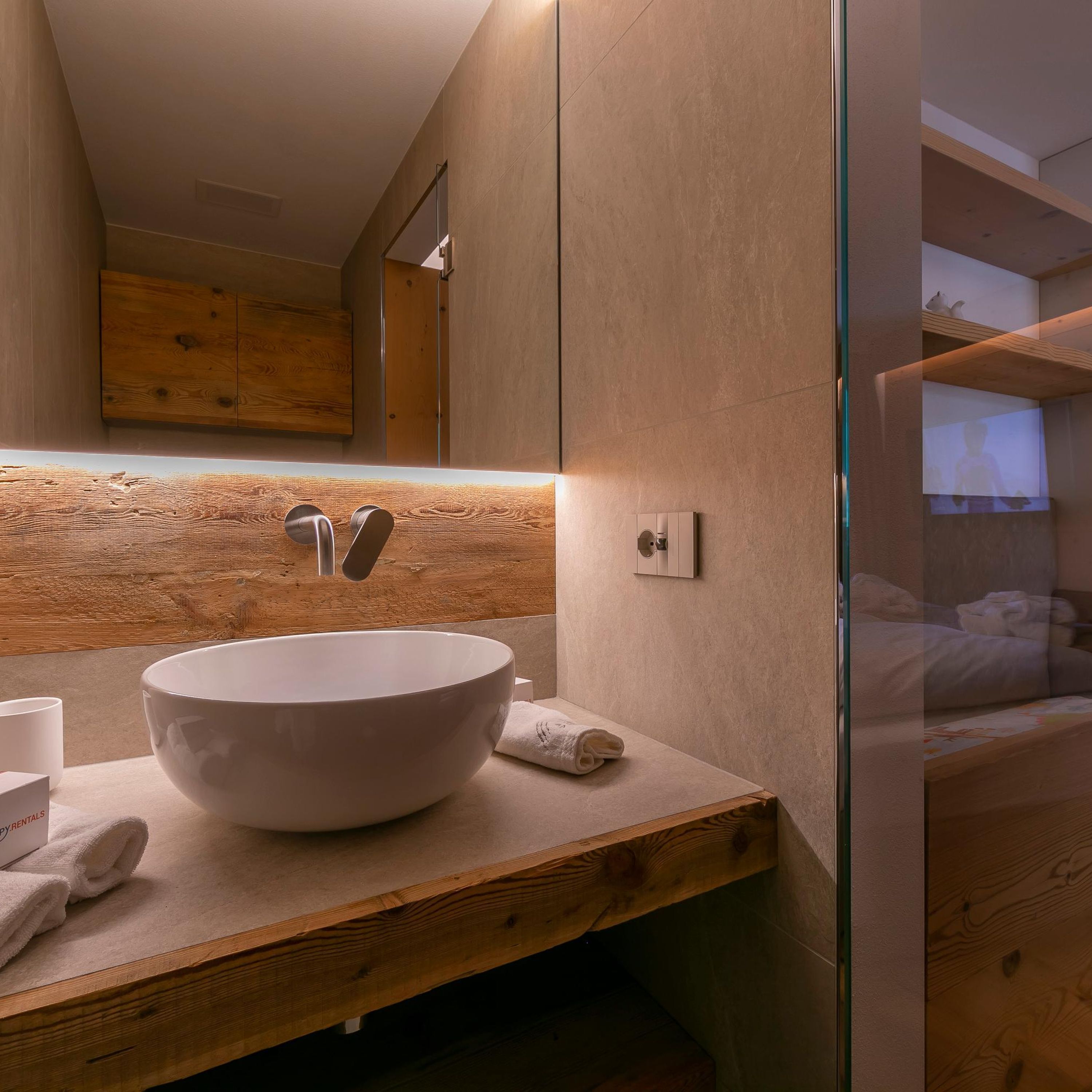 A modern bathroom with a large white sink, wooden countertop, and a glass shower enclosure.