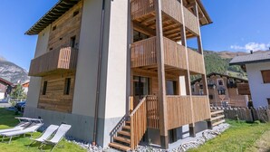 Une maison en bois à deux étages, dotée d’un balcon, d’un escalier et d’un petit jardin.