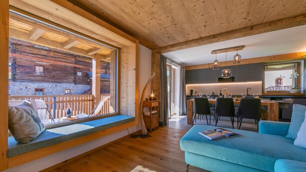 L’intérieur chaleureux d’un chalet avec un plafond en bois, un coin repas avec une cuisine, et une grande fenêtre donnant sur une terrasse en bois.