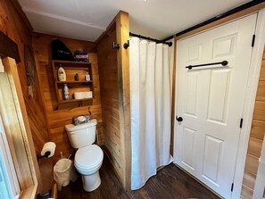 Un bagno in legno con un WC, uno scaffale con articoli da toilette e una porta bianca.