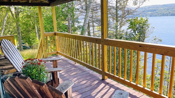 A wooden deck with a railing overlooking a lake, surrounded by trees. - Lakefront Cabin on Rangeley Lake: Sauna & views (Rangeley)