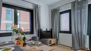 A modern dining area with a wooden table set for a meal, a television, and large windows with curtains. - Boutique Apartment 5 (Lugano)