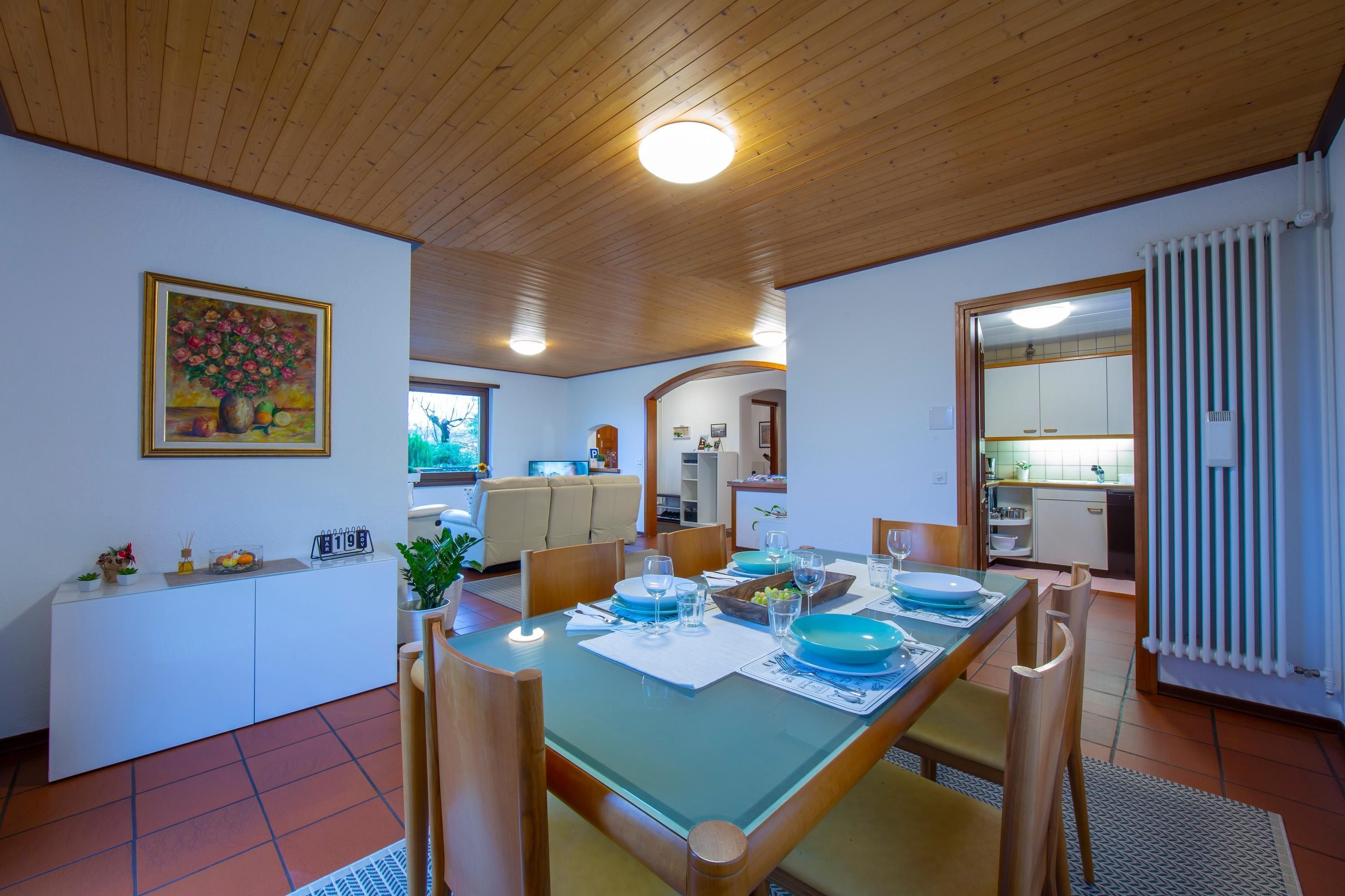 A dining area with a wooden ceiling, a white console table, and a glass-top dining table set for four.