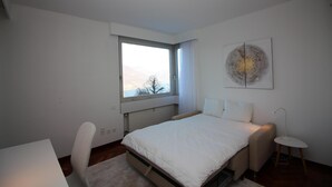 Ein Schlafzimmer mit Bett, Schreibtisch, Stuhl, Fenster und einem Wandbild.