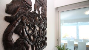 Eine detaillierte HolzSchnitzerei an einer Wand, ein Blumentopf und ein Blick in einen Essbereich mit weißen Stühlen und einem Tisch.