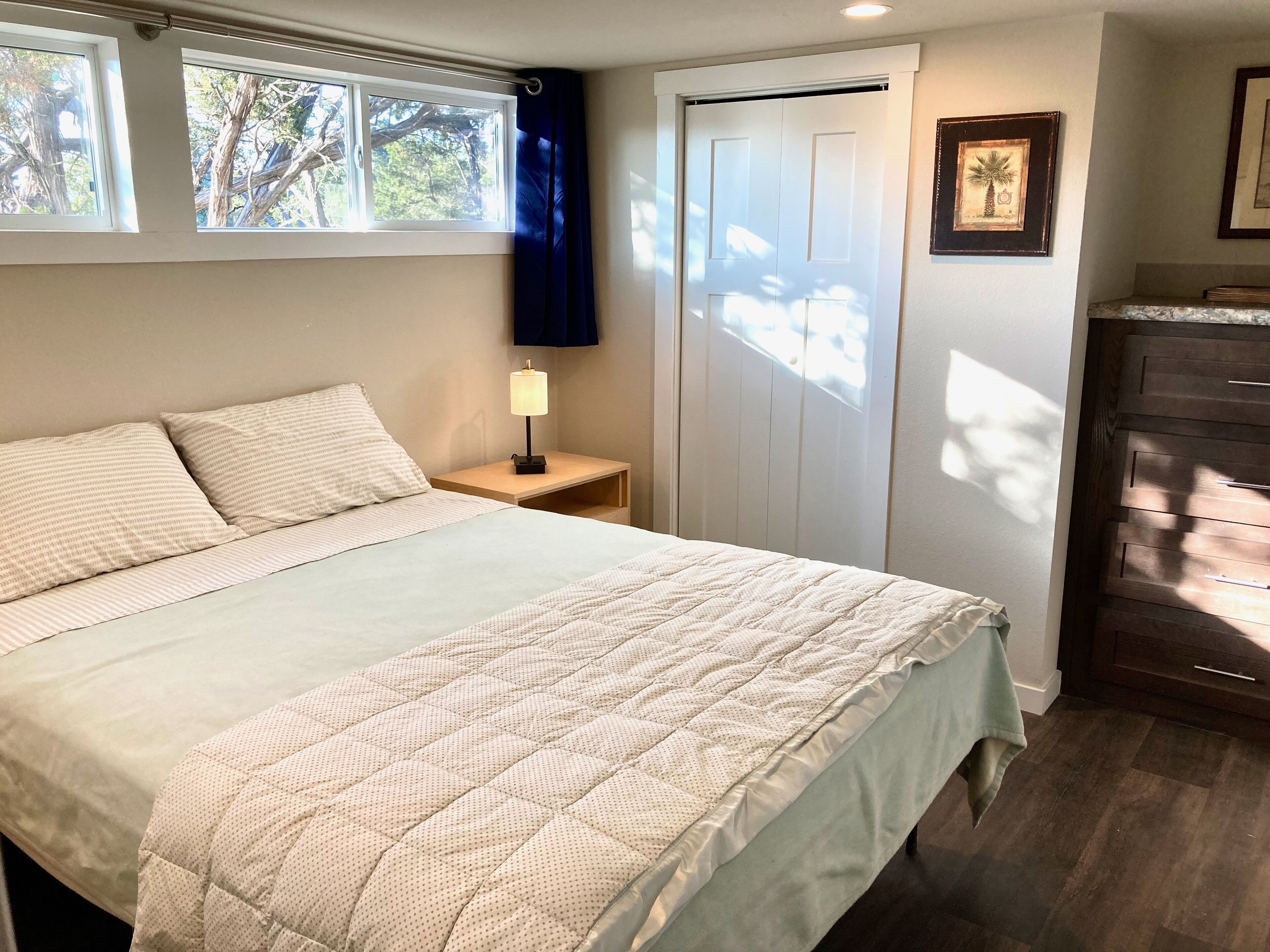 A bedroom with a bed, nightstand, lamp, and a door with a view of trees.