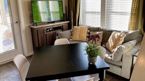 A living room with a TV on a stand, a sofa, a coffee table, and a door with a view. - Cozy Tiny Home in the Hills (Fischer)