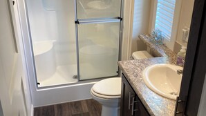 A modern bathroom with a glass-enclosed shower, a white toilet, a sink, and dark wooden flooring. - Cozy Tiny Home in the Hills (Fischer)