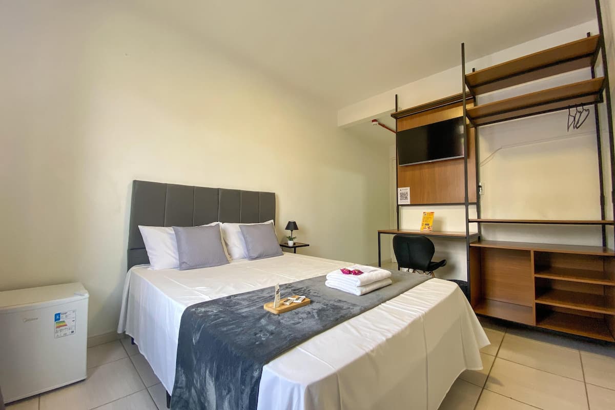 Une chambre d’hôtel comprenant un lit, un bureau, une chaise, une armoire et une petite table avec une serviette et un livre.