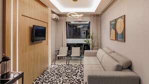 Une chambre d’hôtel moderne équipée d’un canapé, d’une télévision, d’un coin repas avec des chaises et d’un tapis à motifs.