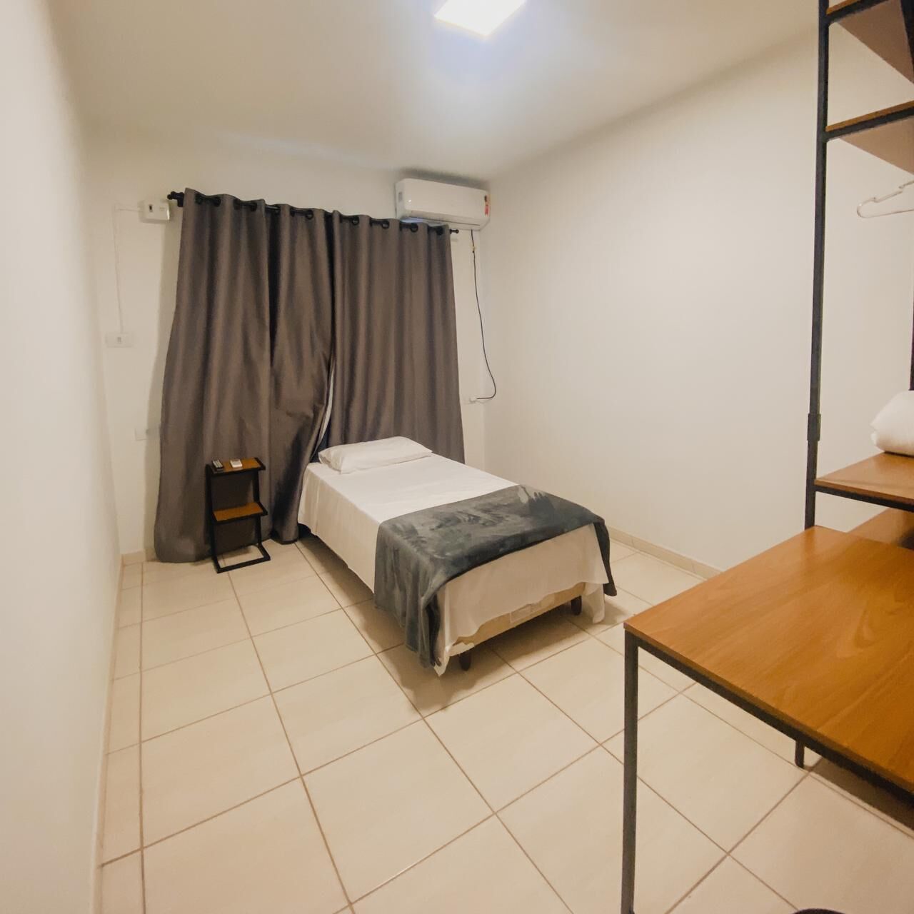 Een kleine, schone kamer met een bed, een tafel en een plank.
