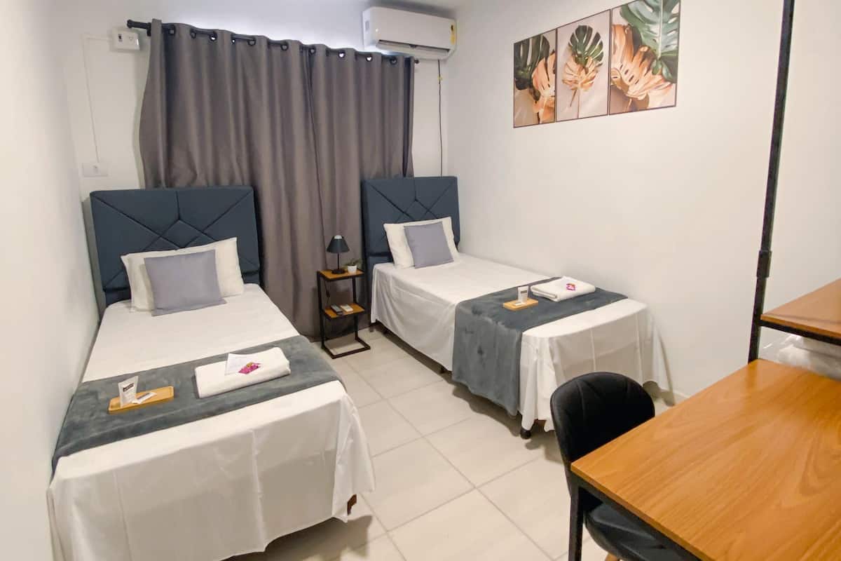 Une chambre d’hôtel avec deux lits simples, une petite table, une chaise et un bureau.