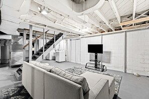 Een ruime kamer met een bank, een flatscreen-tv en een trap naar een hoger gelegen verdieping.