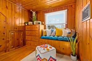 Een gezellig chaletinterieur met houten wanden, een bank met kussens, een dressoir en een potplant.