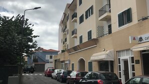 Un immeuble à plusieurs étages doté de balcons, d’un café et bordé de voitures garées le long de la rue.