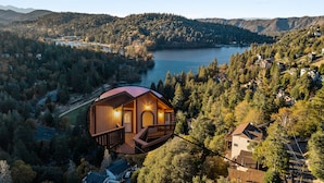 En husbåd med træterrasse og balkon, omgivet af skov og sø.