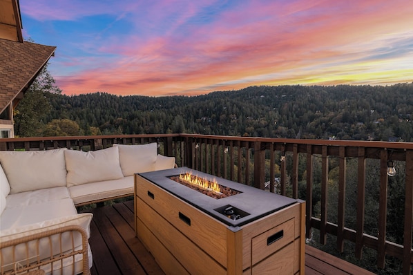 A deck with a built-in fire feature, a sofa, and a view of a forested hillside.