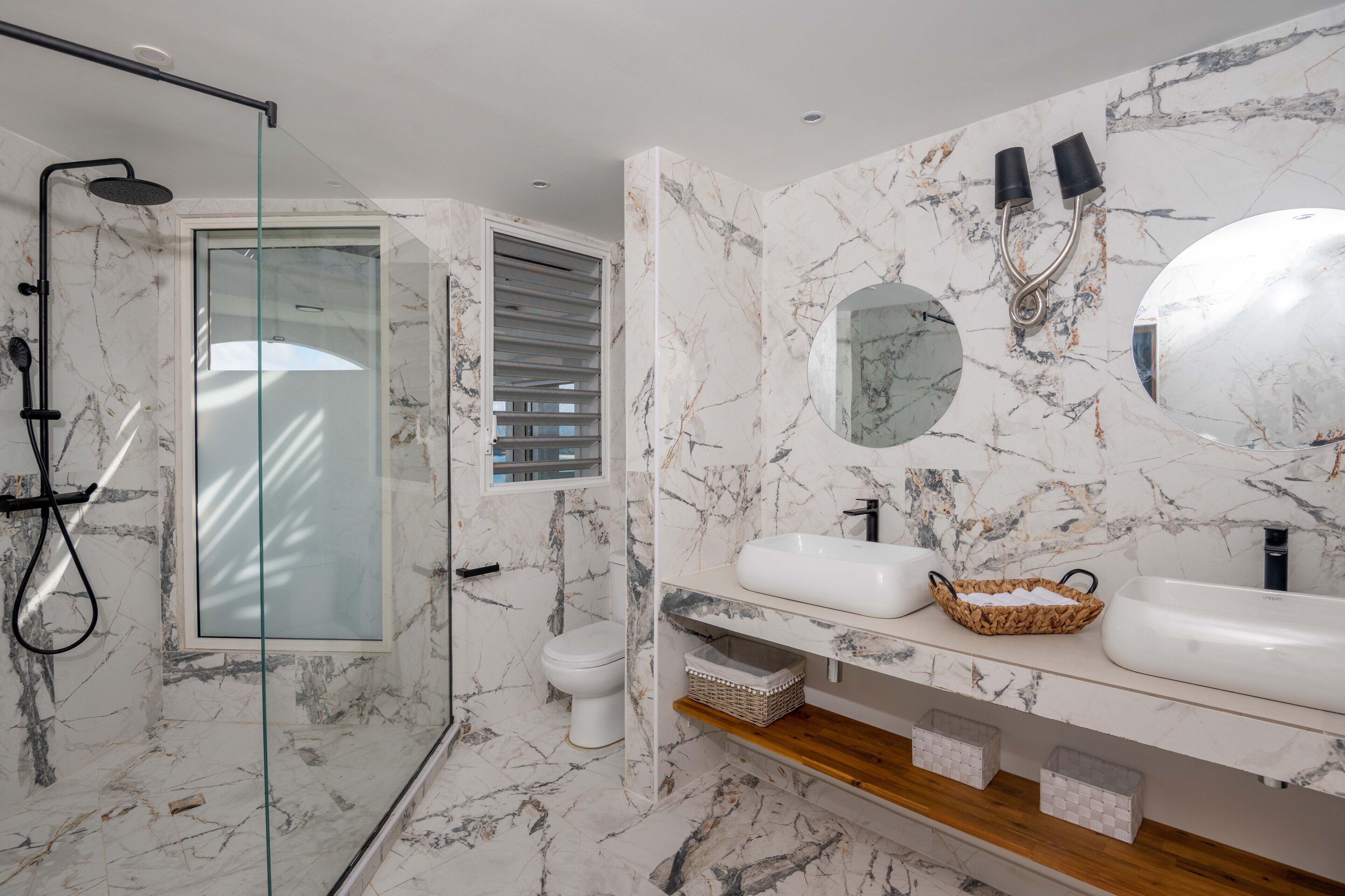 A modern bathroom with a glass-enclosed shower, a toilet, and a vanity with two sinks and a large mirror.