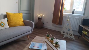 A living room with a grey sofa, yellow cushions, a small table with a magazine, a decorative mirror, and a Christmas tree. - Le Sunny - Spacious, renovated duplex apartment (Outreau)