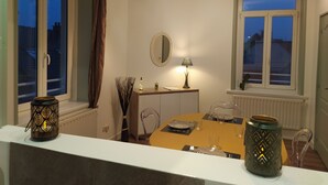 A dining area with a table set for two, a mirror, a lamp, and a window with curtains. - Le Sunny - Spacious, renovated duplex apartment (Outreau)