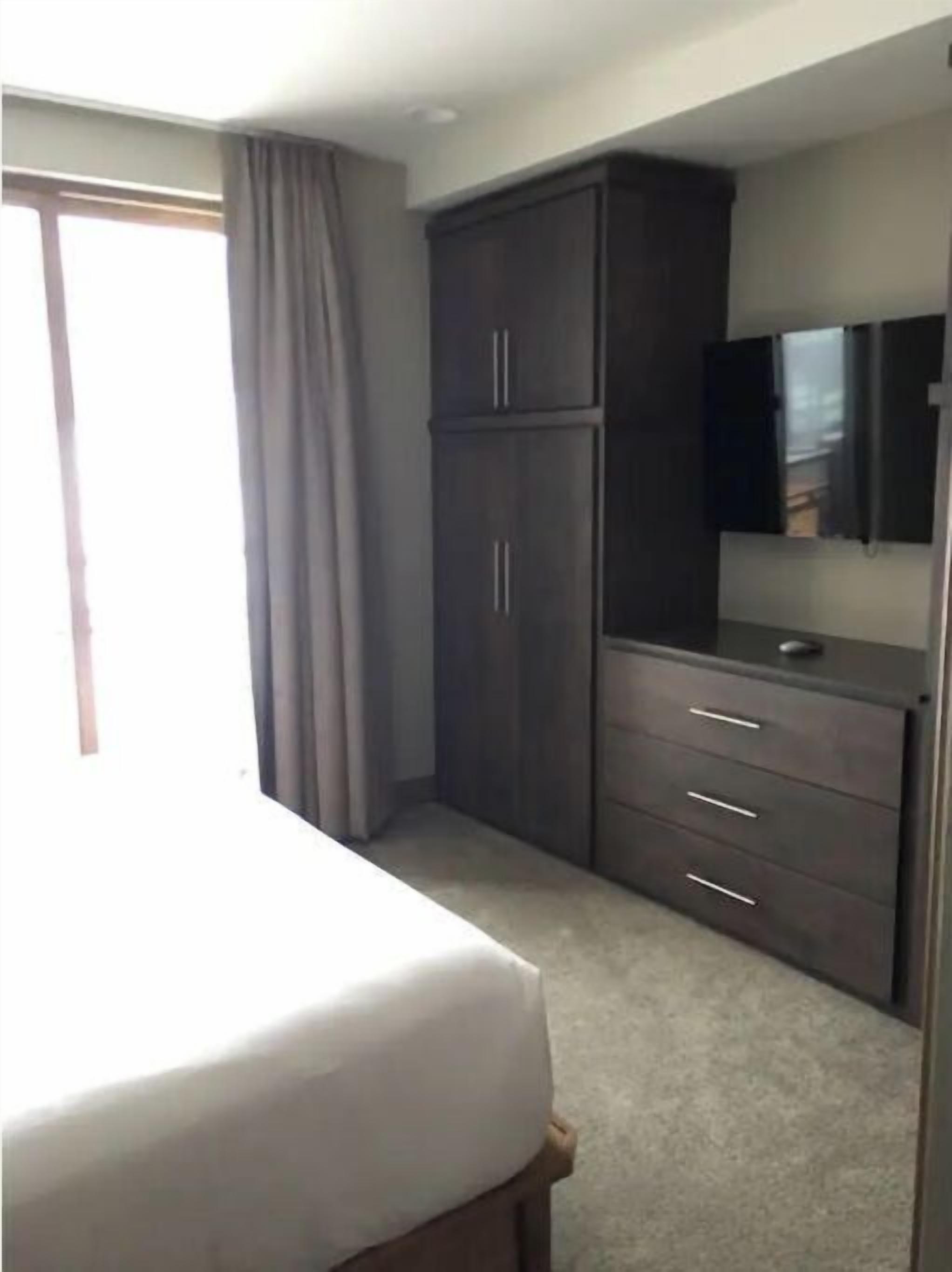 Een slaapkamer met een bed, een kledingkast, een televisie en een raam met gordijnen.