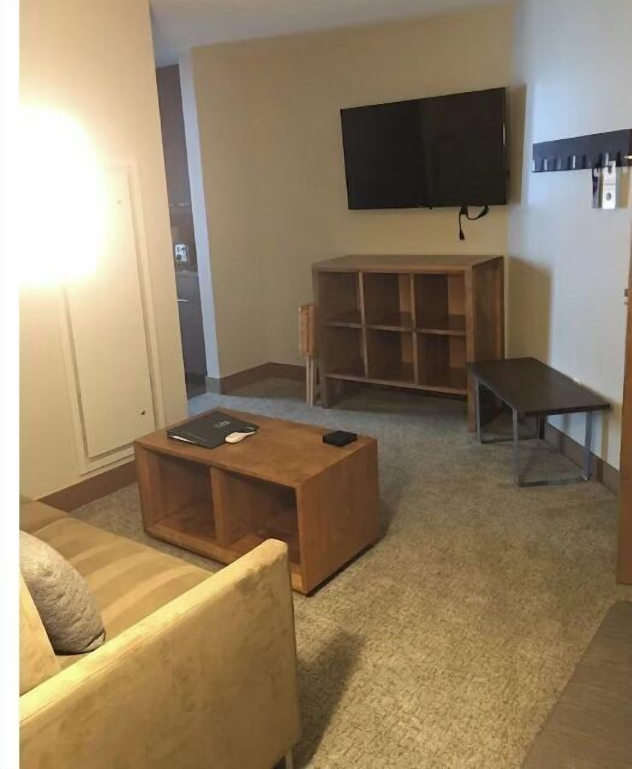 A living room with a wooden coffee table, a sofa, a TV mounted on the wall, and a bookshelf.