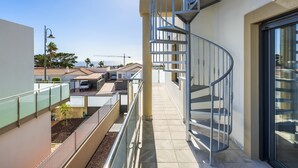 Ein modernes Gebäude mit Wendeltreppe, einem Balkon mit Geländer und Blick auf das Meer sowie Baukräne im Hintergrund.