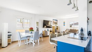 Eine moderne Küche mit Kochinsel, ein Essbereich mit weißen Stühlen und ein Wohnbereich mit Sofa und Couchtisch.