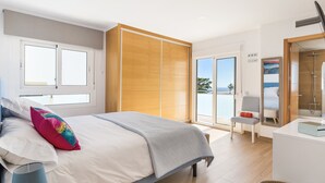 Ein modernes Schlafzimmer mit einem Bett, einem Sessel, einem Schreibtisch und einer Schiebetür, die auf einen Balkon führt.