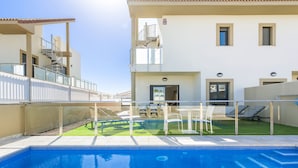 Ein Swimmingpool mit klarem, blauem Wasser, einer Glasbrüstung und einer kleinen Terrasse mit weißen Stühlen und einem Tisch.