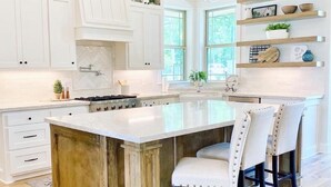 A spacious kitchen with white cabinetry, a large island with bar stools, and pendant lighting. - Luxury Farmhouse with Pool - Perfect for Groups (Conroe)