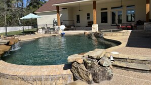 A backyard with a swimming pool, stone steps, and a covered patio area. - Luxury Farmhouse with Pool - Perfect for Groups (Conroe)