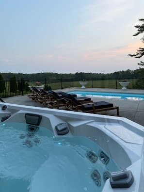 A hot tub with lounge chairs and a pool, surrounded by a fence and trees. - Stunning Historic Maine Stone Castle (Bath)