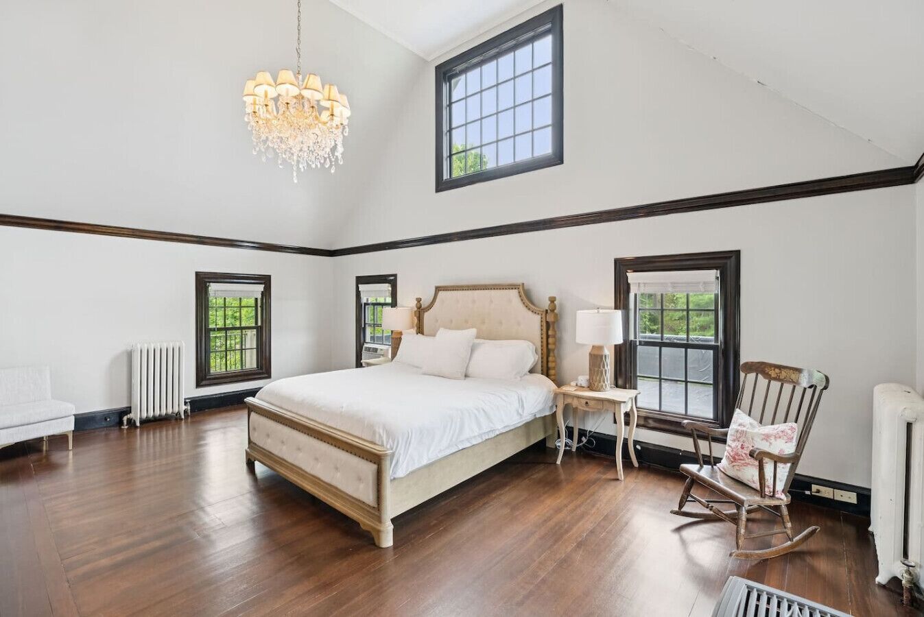 A spacious bedroom with a large bed, a chandelier, and multiple windows.