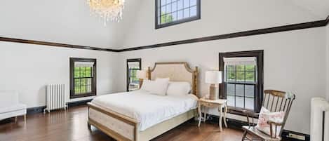 A spacious bedroom with a large bed, a chandelier, and multiple windows.